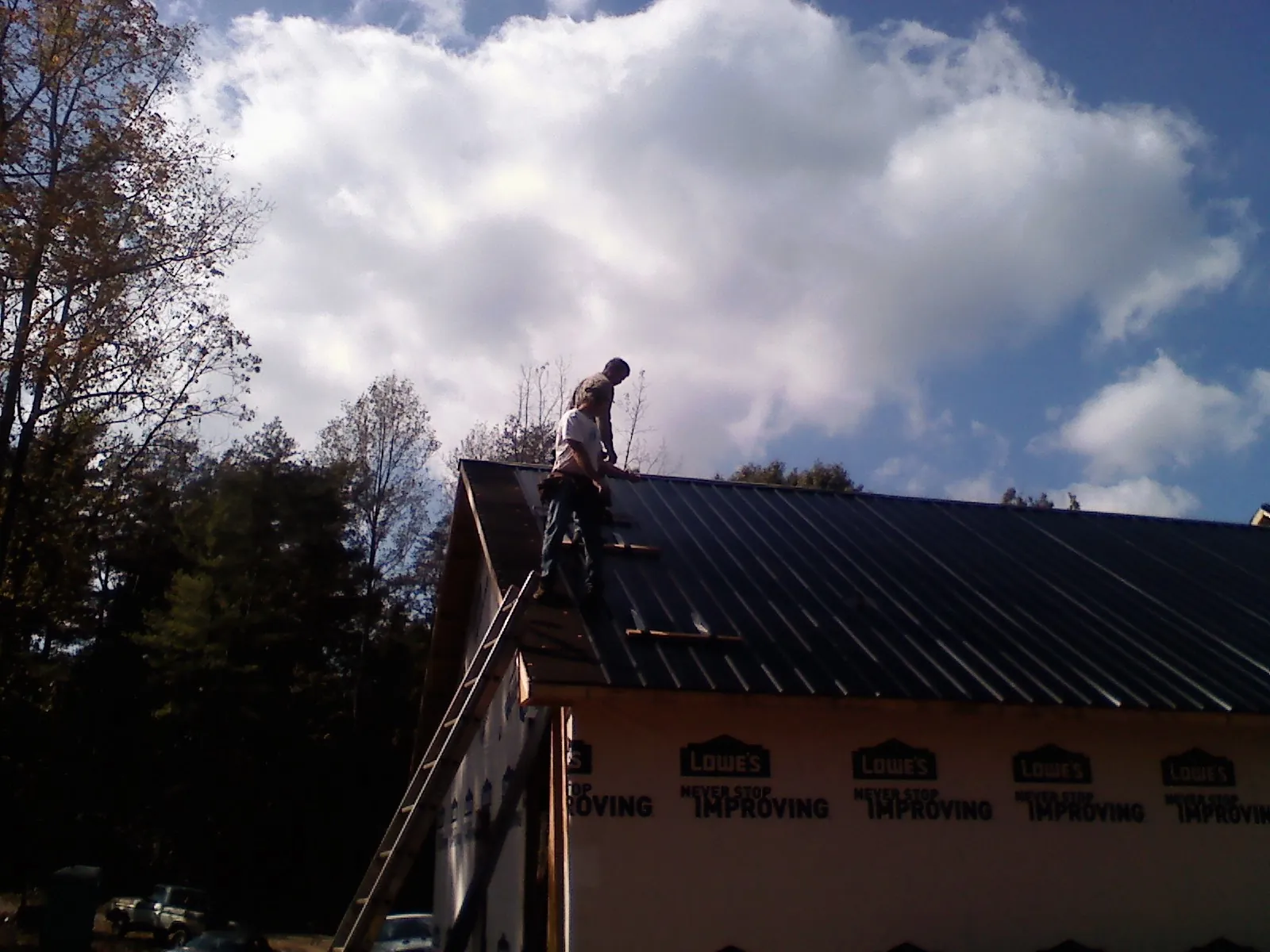 Roofer fastening dark metal panels high against a cloudy sky, from a Roof Inspection job in Wonalancet