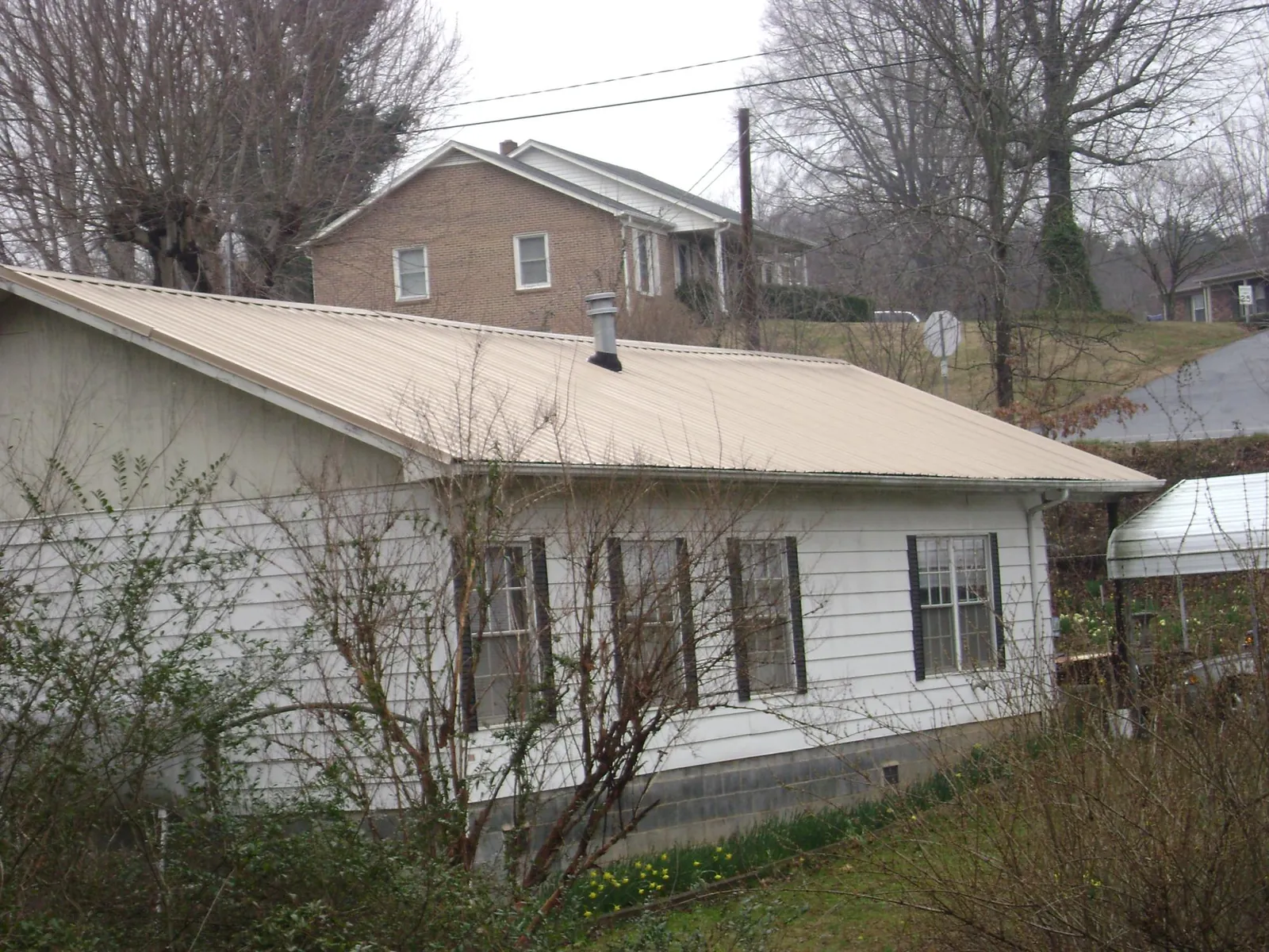 Tan metal roof on a white sided house set into a hillside — Commercial Roofing by Roofing Brothers in Wonalancet